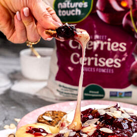 Hand dipping a cracker into cherry chia baked brie.