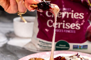 Hand dipping a cracker into cherry chia baked brie.