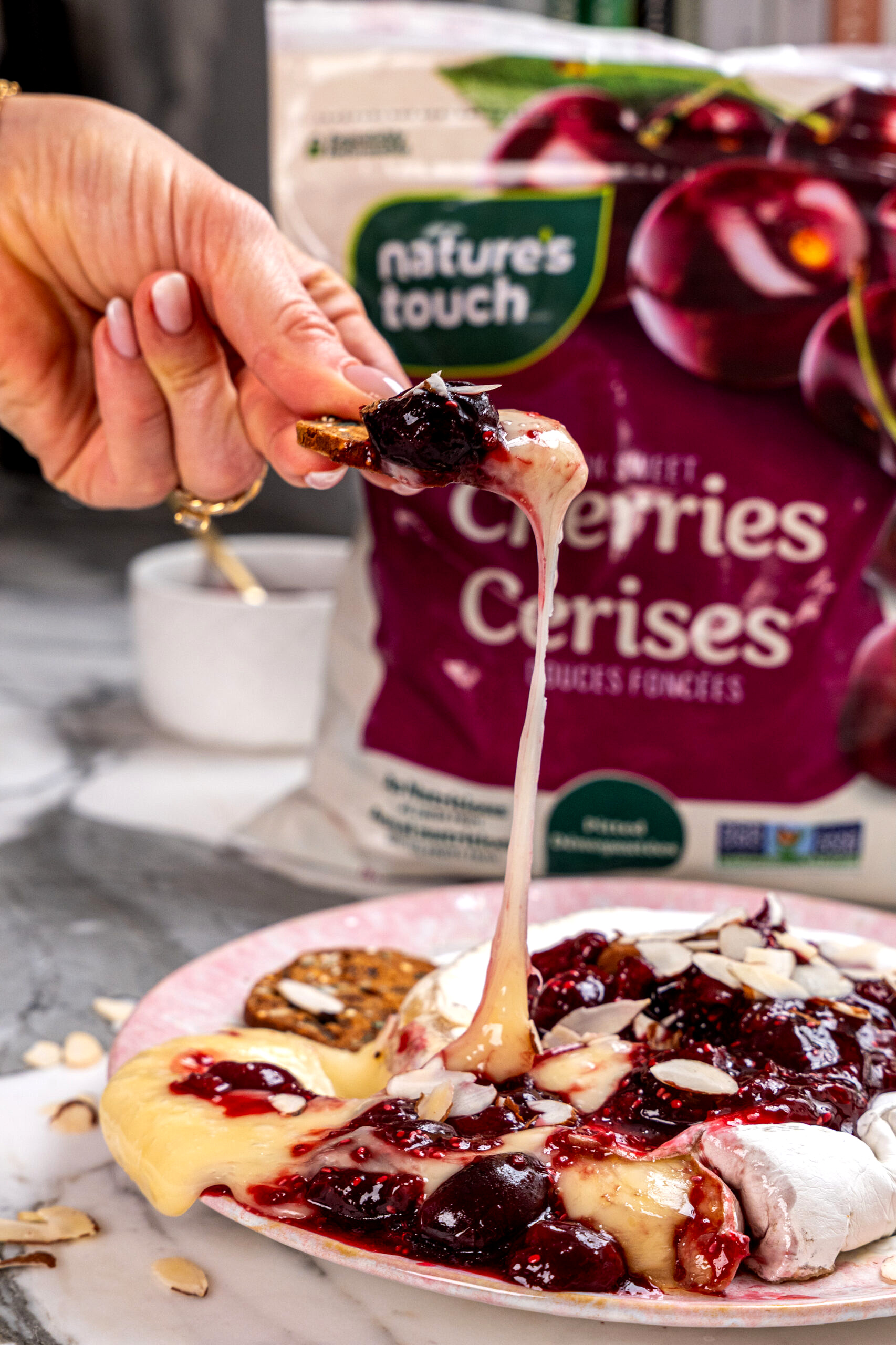 Hand dipping a cracker into cherry chia baked brie.