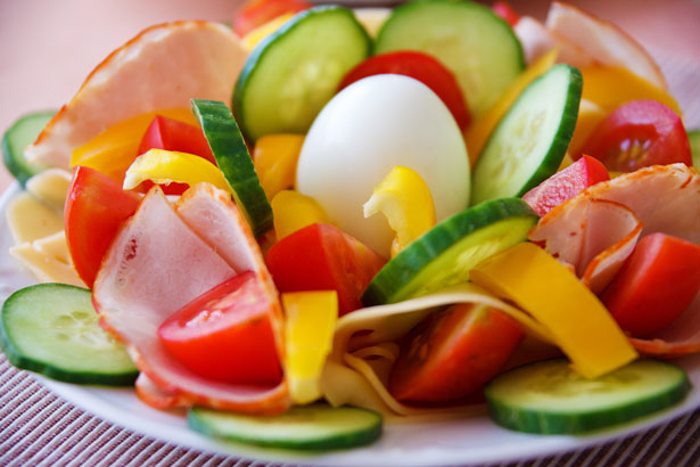 cut fruits and vegetables around an egg on a white plate