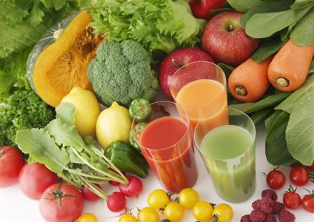 A tableful of fruits and vegetables with three glasses of juice.