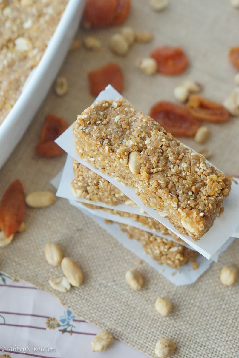 A stack of gluten free no bake granola bars with peanut butter and apricot with parchment paper in between with nuts around.