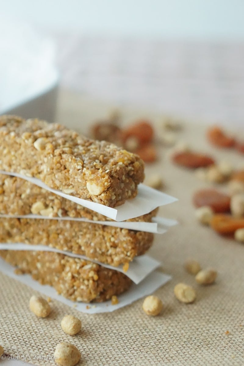 A stack of four gluten free no bake granola bars with peanut butter and apricot with parchment paper in between with nuts in the background.