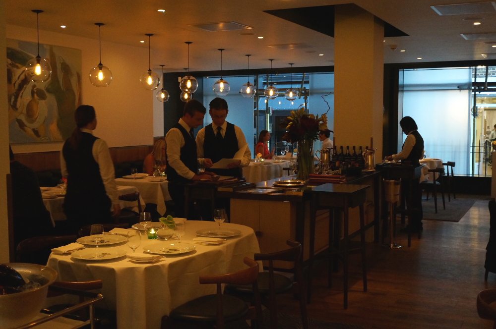 Inside of a restaurant with waiters standing. 